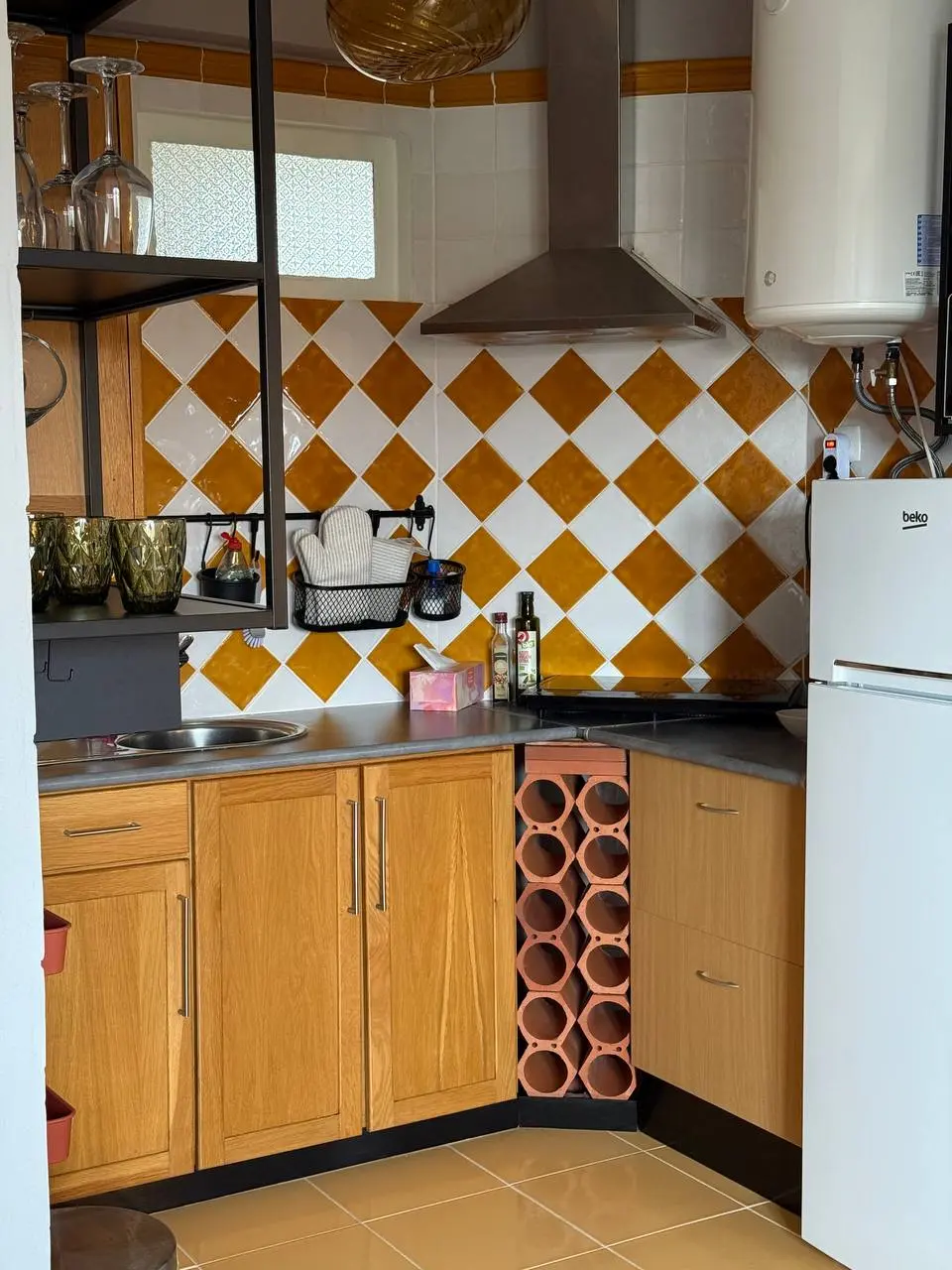 Compact L-shaped kitchen with wood cabinets, white fridge, and orange-and-white tiled backsplash