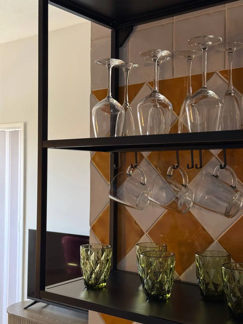 Open shelf with wine glasses, mugs, and green tumblers above the kitchen counter