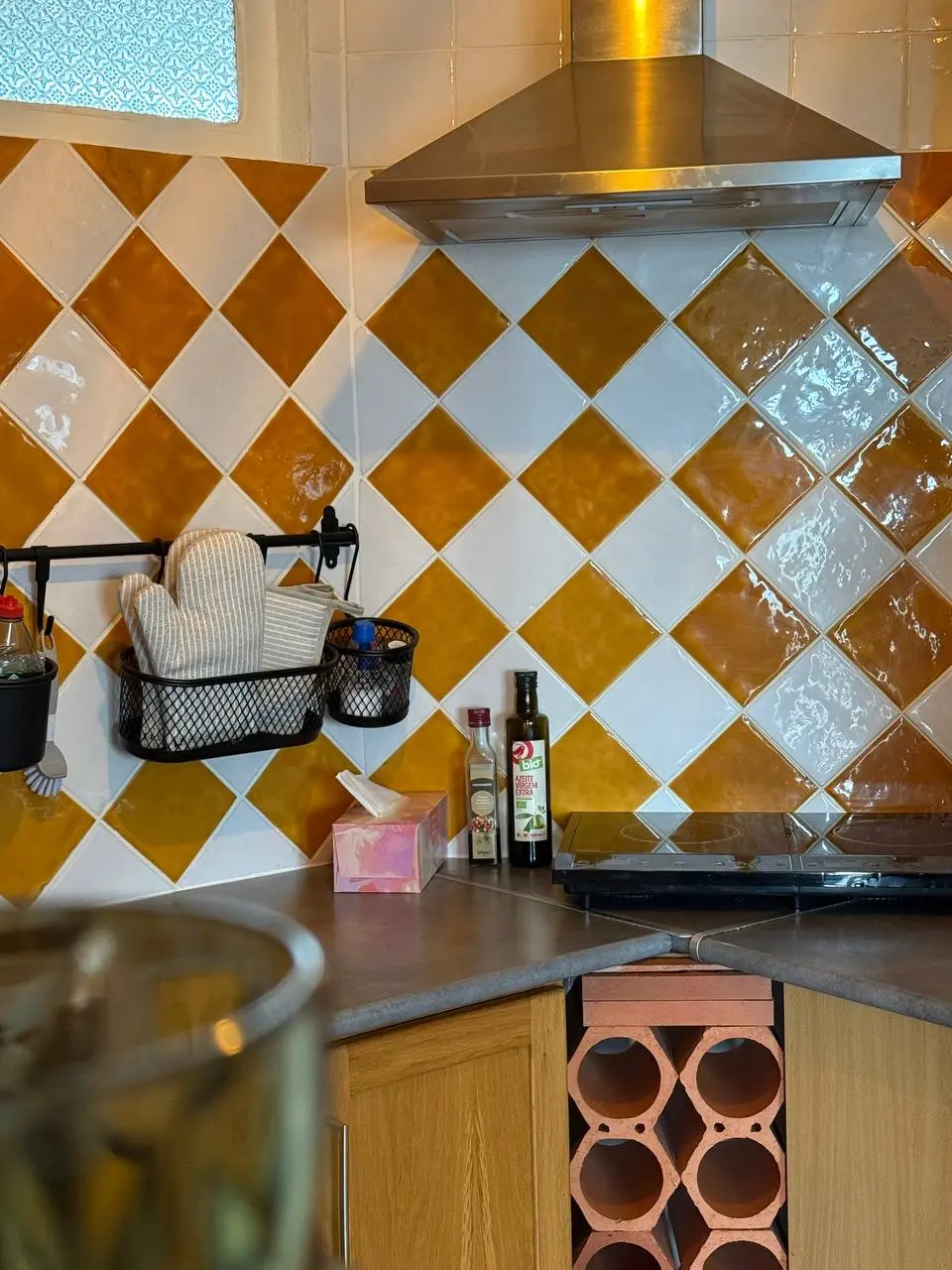 Kitchen counter corner with extractor hood, cooktop, oven mitts, and tiled backsplash