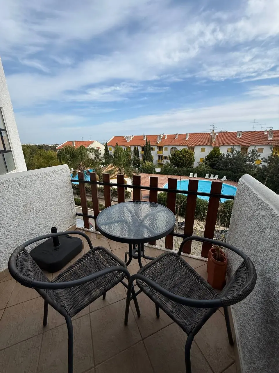 Private balcony with two chairs and a round table overlooking the pool and neighboring buildings