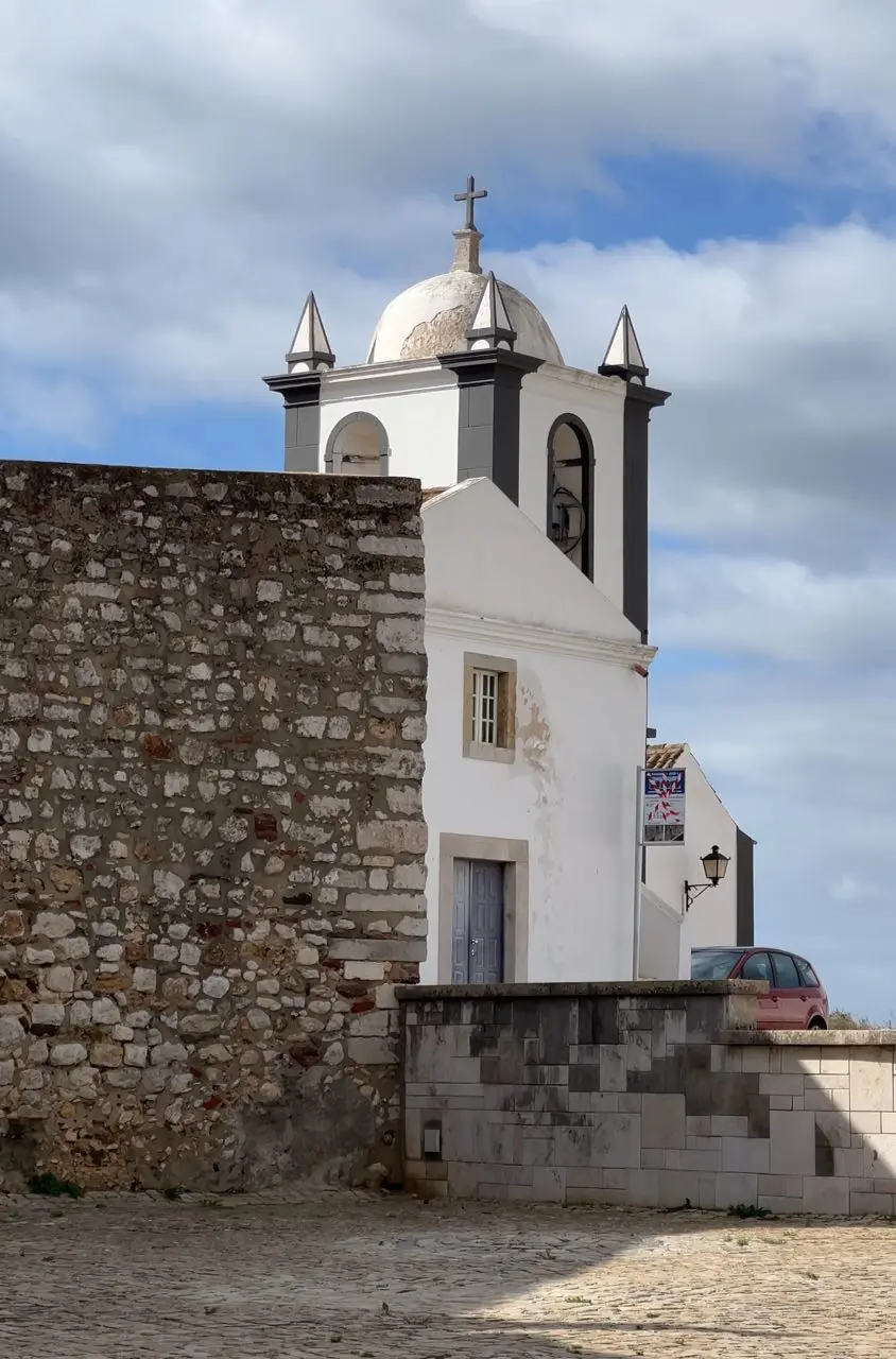 White church tower and old stone wall in a historic Algarve village square