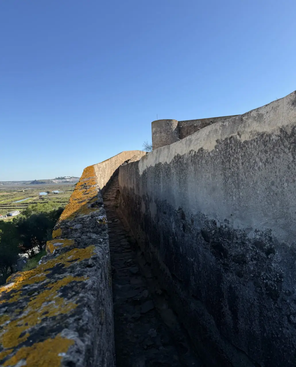 Narrow stone walkway on top of a fortress wall with marshland beyond